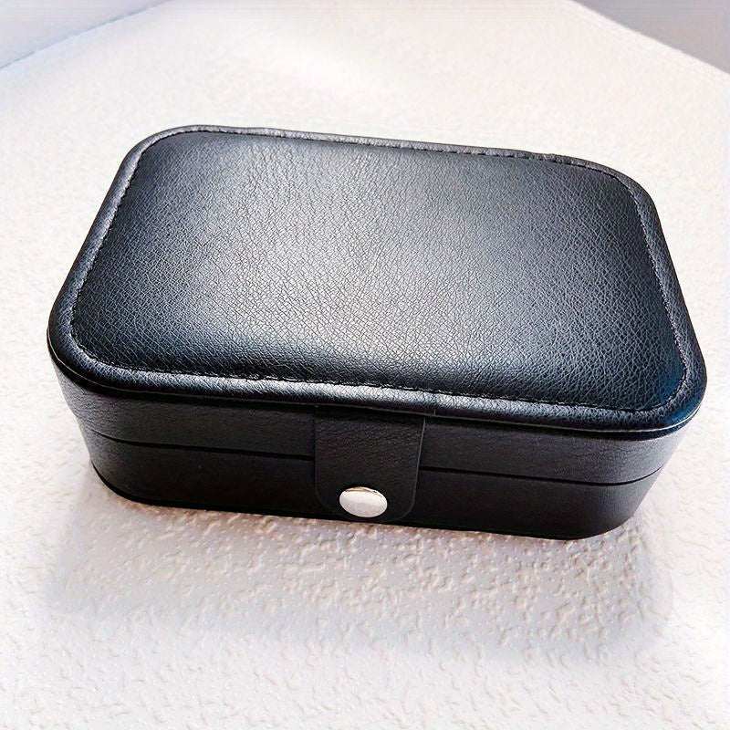 Black leather portable jewelry travel case with button closure and rectangular shape on a white surface