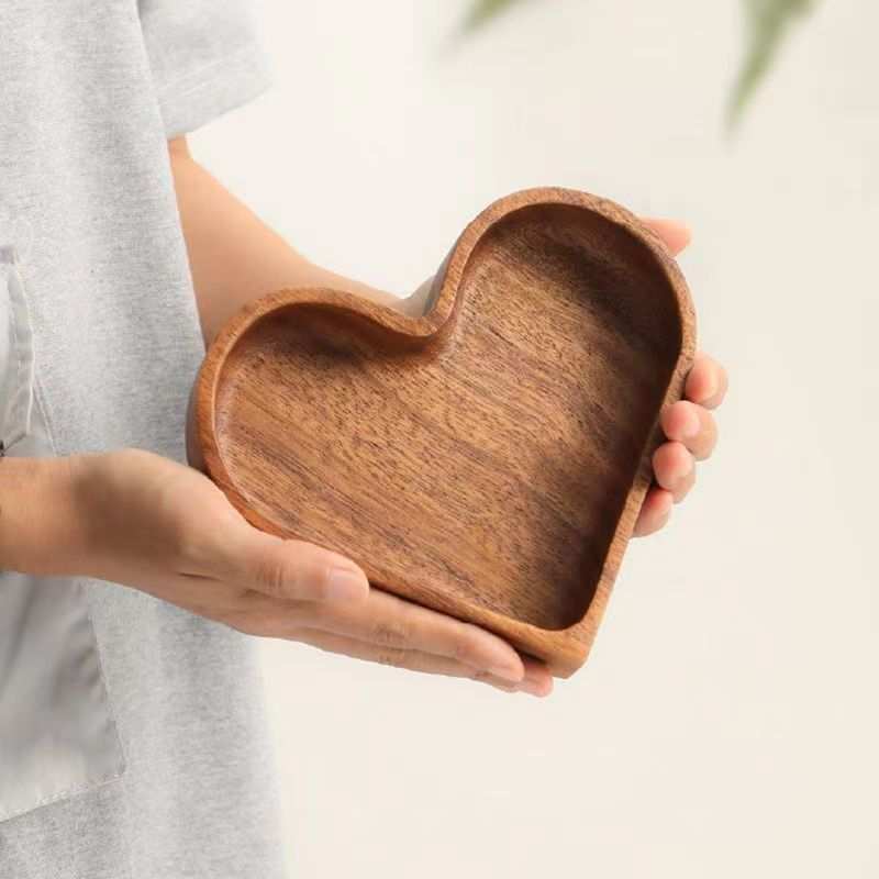Heart-shaped walnut-colored wooden tray held in hand for serving dried fruits and appetizers