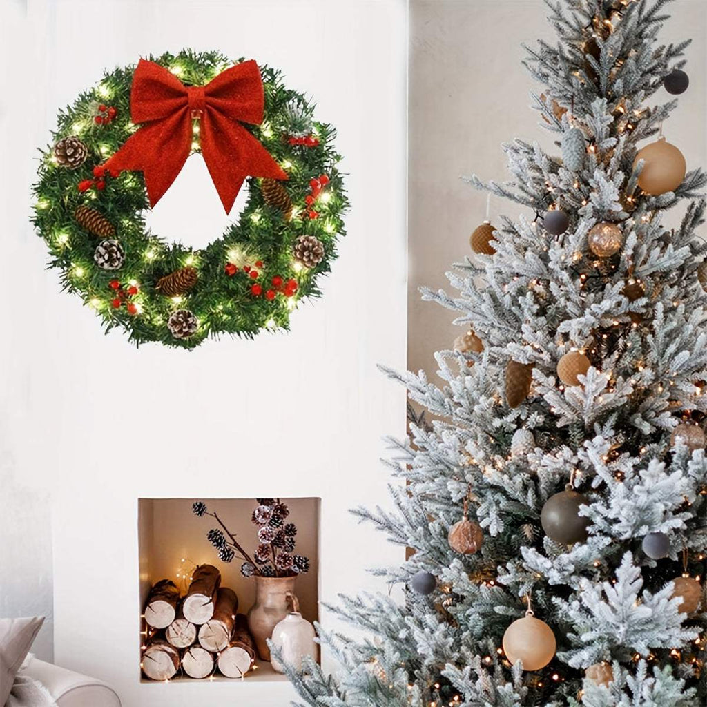 20 inch pre-lit Christmas wreath with red bow, pine cones, berries, and lights hanging on white wall next to decorated Christmas tree