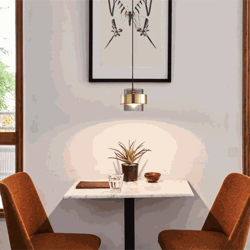 Modern bedroom art decor pendant light with LED bulb hanging above a small dining table with brown chairs and wall art background