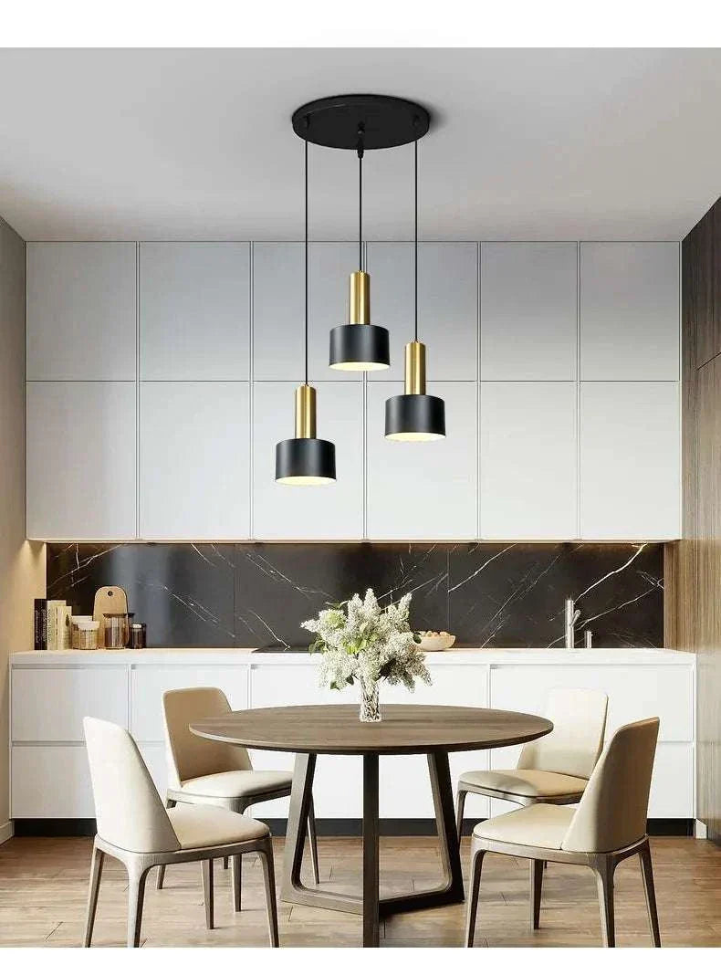 Nordic simple three-chandelier lamp with black and gold pendants over a modern dining table in a minimalist kitchen