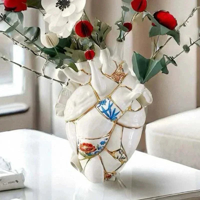 Ceramic vase shaped like anatomical heart with painted floral details and red and white artificial flowers on white table