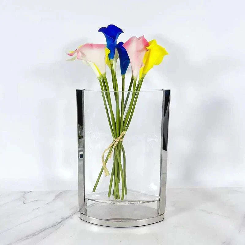 Modern glass vase with metal frame holding colorful artificial flowers on a white surface