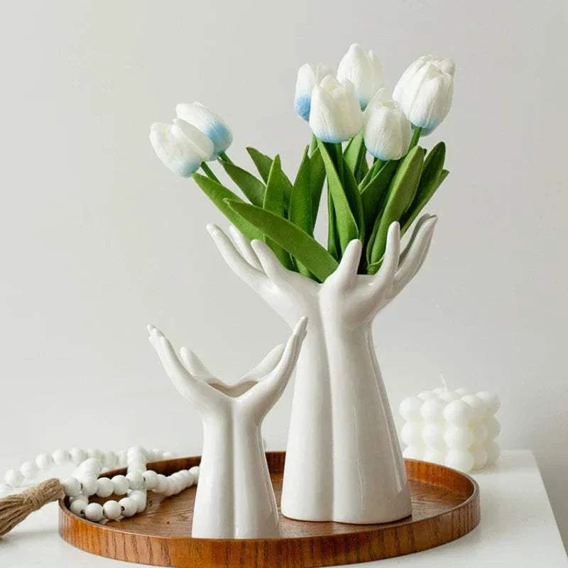 Modern ceramic vase shaped like hands holding a bouquet of white tulip flowers on a wooden tray