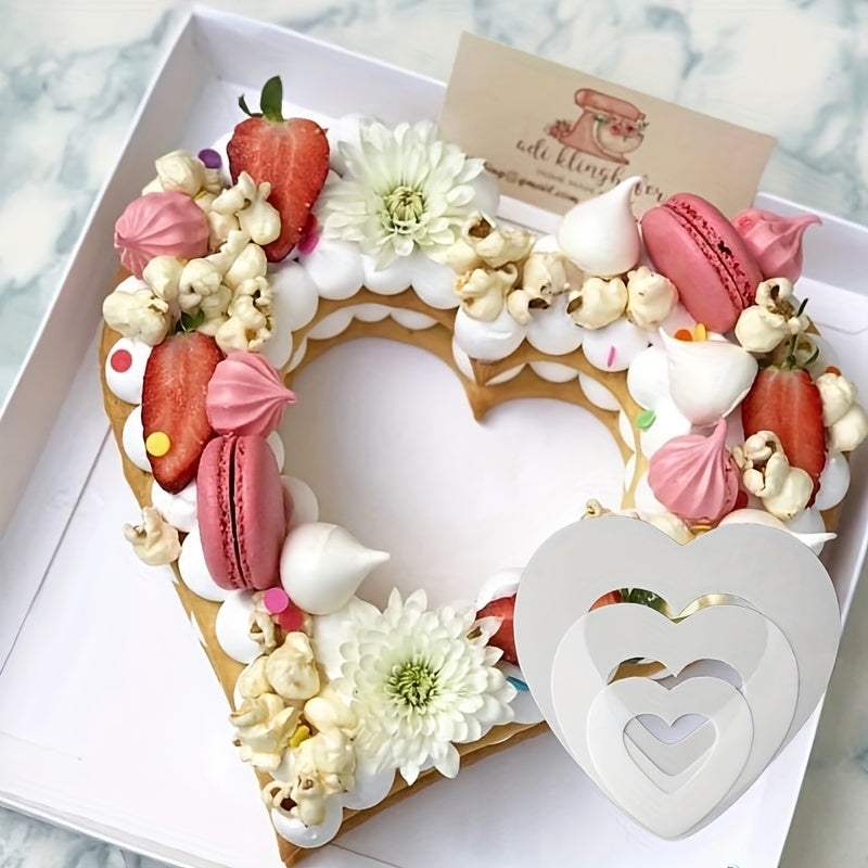 Heart shape cake decorated with macarons, strawberries, popcorn, and flowers with heart shape cake molds in varying sizes on a marble surface